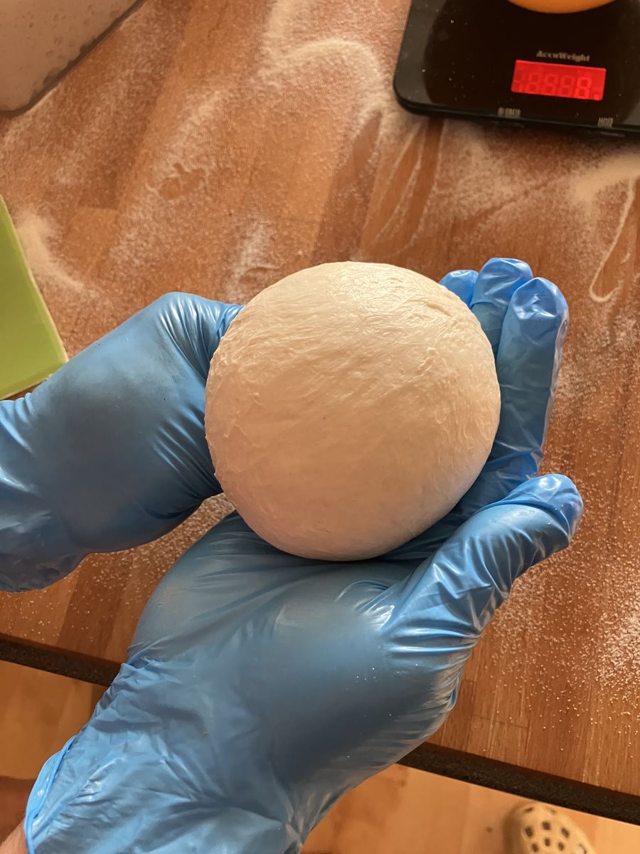 Freshly weighed ball of pizza dough in gloved hands