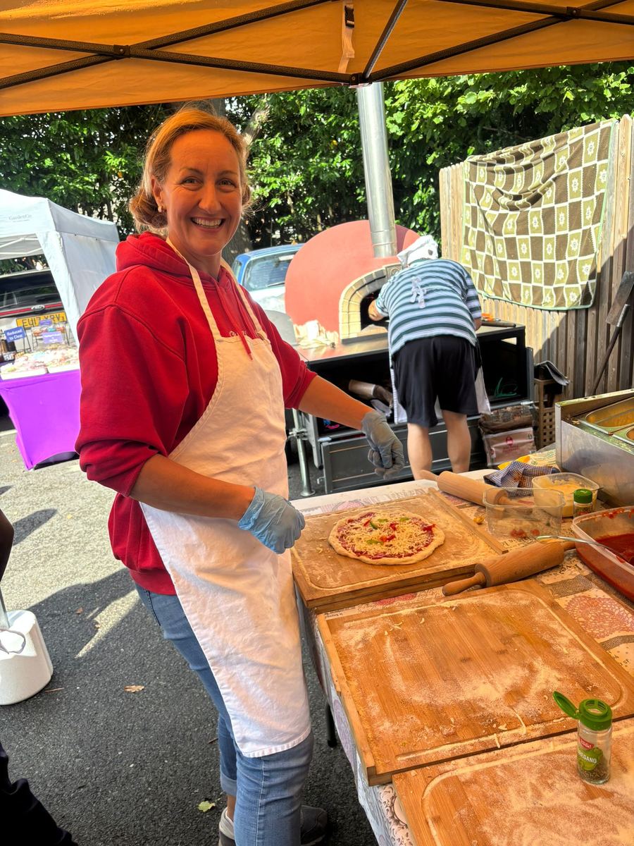 Team member topping a pizza on a wooden peel at the stall