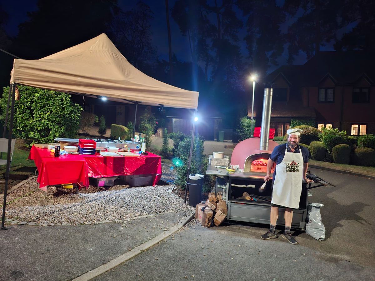 Red dome wood-fired pizza oven glowing at an evening party