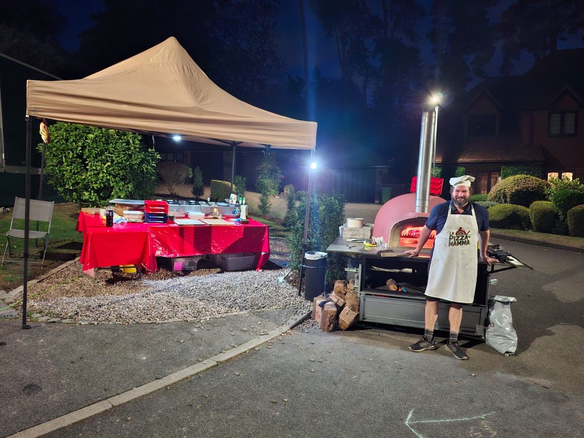 Chef beside the glowing wood-fired pizza oven at an evening event