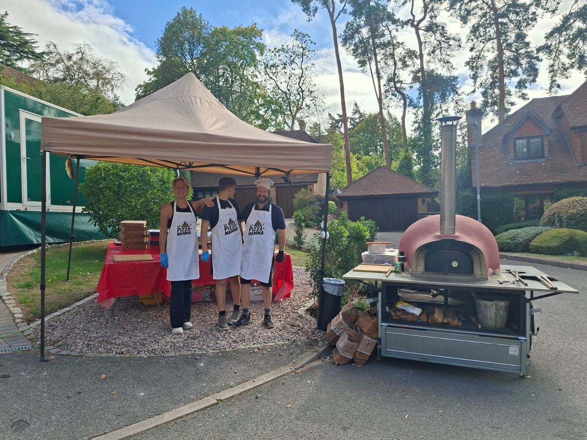 Pizza team posing under a gazebo beside the oven trailer