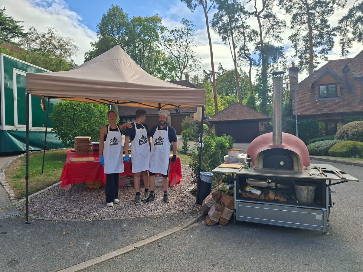 Team under a pop-up gazebo next to a wood-fired pizza oven
